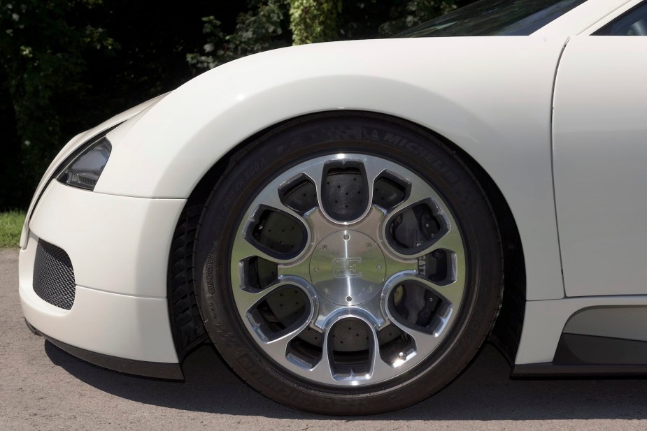 The chrome wheel and Michelin tires on a white Bugatti Veyron, trees visible in the background.