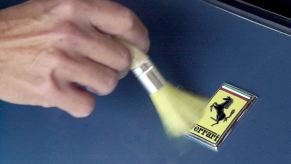 Hand with a brush dusting off a Ferrari logo before a car show