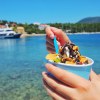 The hands of a woman eating ice cream out of a bowl, a cruise ship parked in a bay in the background.