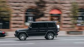 A black Mercedes-Benz G-Class speeds down a city street.