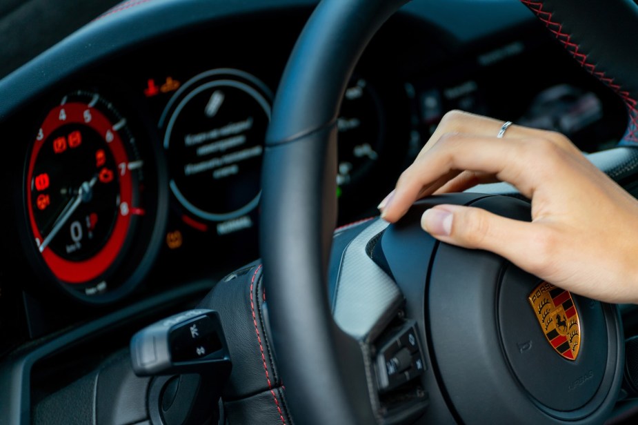 Woman's hand on the steering wheel of a reliable Porsche luxury car.