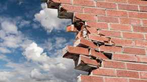 Broken brick wall with bright blue sky visible beyond.