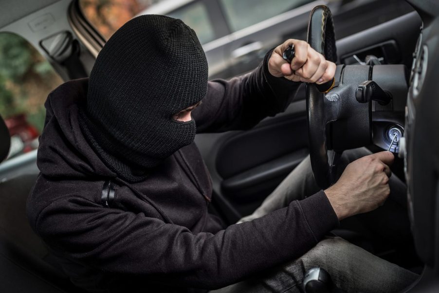 Masked car thief starts a stolen car with a screwdriver.