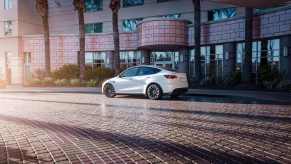 A white Tesla Model X parked next to a large structure.