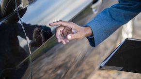 A black car door is dented, with a man from insurance inspecting the damage