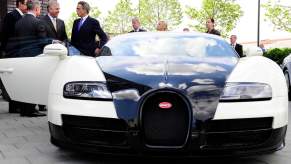 Men in suits stand next to a black and white Bugatti Veyron supercar.