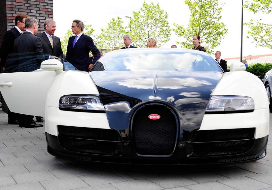 Men in suits stand next to a black and white Bugatti Veyron supercar.