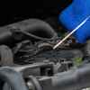 A man's hand holding blue towel and engine oil dipstick in front of open hood in very close view