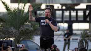 Elon Musk speaking to a crowd in front of a SpaceX craft wearing an "Occupy Mars" t-shirt