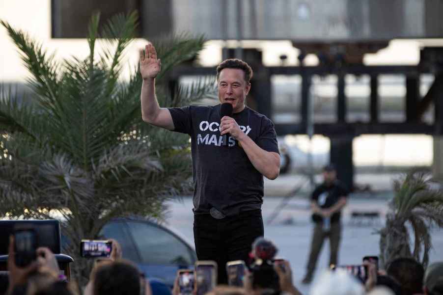 Elon Musk speaking to a crowd in front of a SpaceX craft wearing an "Occupy Mars" t-shirt