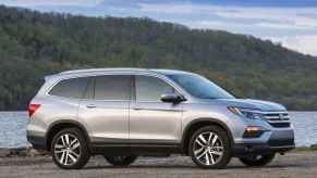 A silver 2016 Honda Pilot parked in right profile view in front of water and a mountain