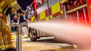 A fire hydrant being used by a firefighter, with a fire truck parked in front of it