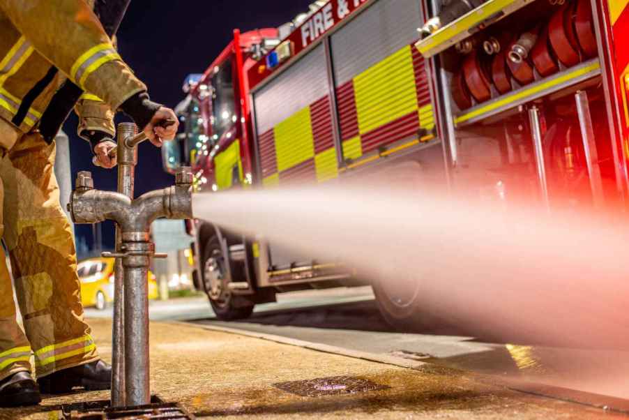 A fire hydrant being used by a firefighter, with a fire truck parked in front of it