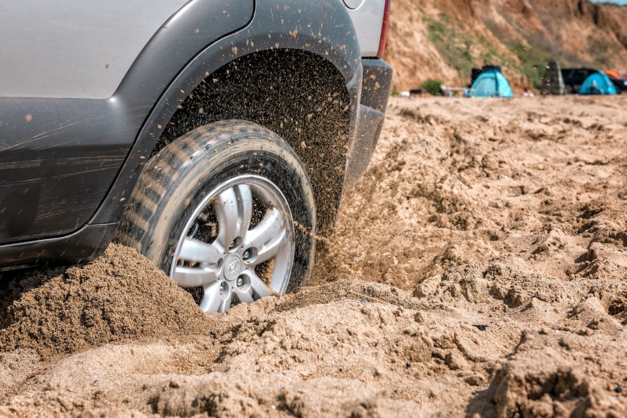 An SUV tire spinning in beach sand