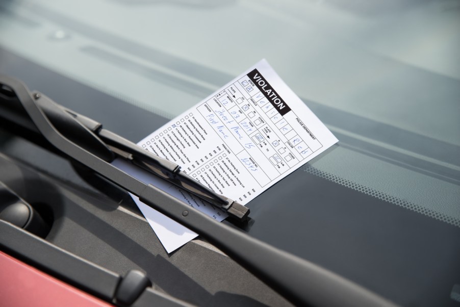 A parking ticket pinned onto a car's windshield by a windshield wiper