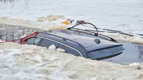 The roof of a car submerged in a frozen lake with rescue equipment surrounding the sit