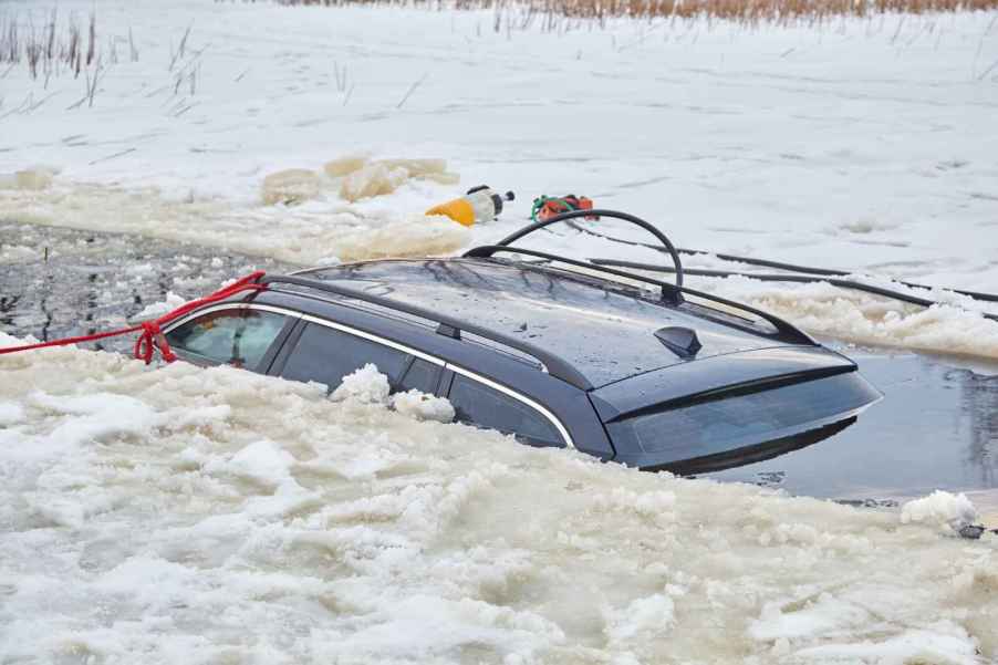 The roof of a car submerged in a frozen lake with rescue equipment surrounding the sit