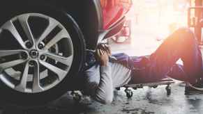 Mechanic in denim overalls lays under a car's front end