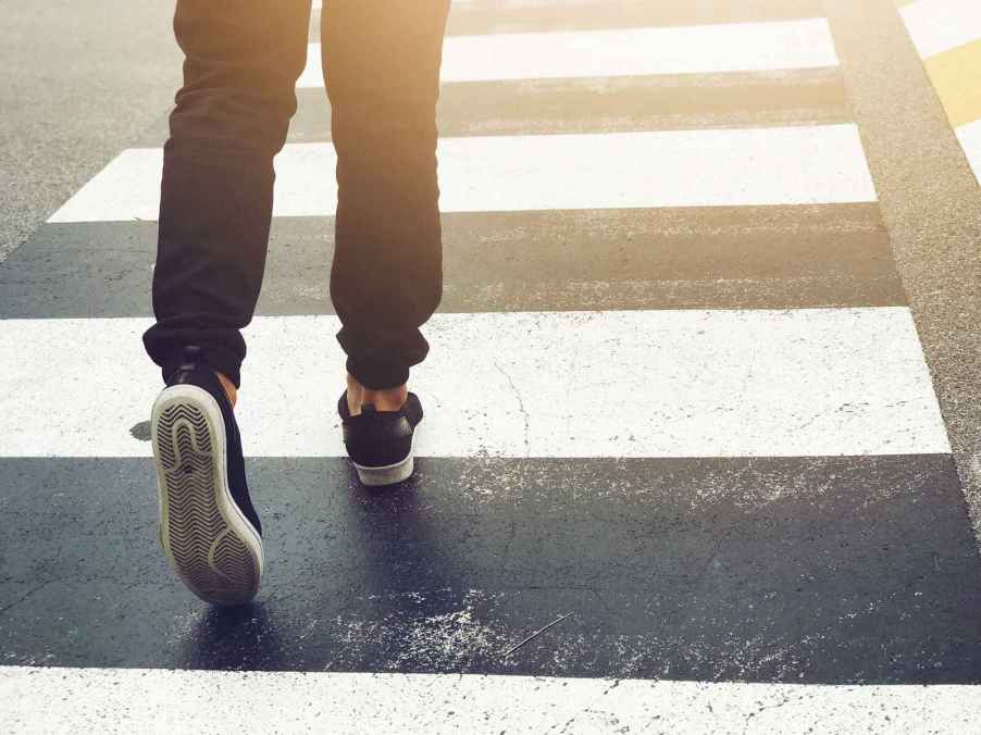 A pedestrian crossing the street using a crosswalk legs only shown