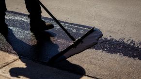 A man pushing a flatbrush to evenly distribute sealcoating on a road