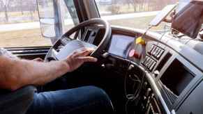 A semi-truck driver shown from neck down driving his rig