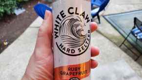 A man's hand holding a White Claw hard seltzer can up to the camera