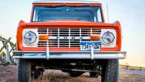 Orange 1972 Ford Bronco parked in a field, the sky visible in the background.