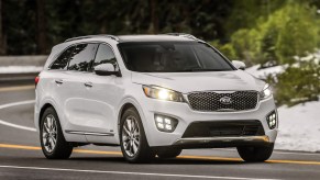 A white 2016 Kia Sorento driving in right front angle view with headlamps illuminated