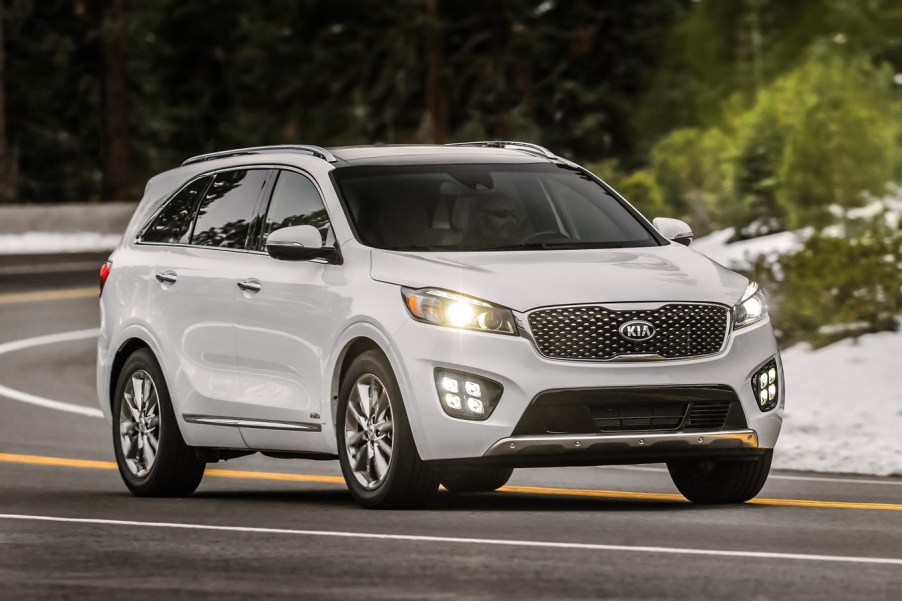 A white 2016 Kia Sorento driving in right front angle view with headlamps illuminated