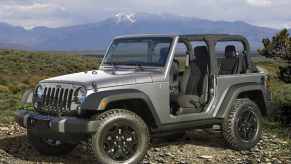 A silver 2018 Jeep Wrangler parked outside with its rag top off in left front angle view