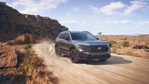 A dark metallic 2023 Honda CR-V Sport driving on a dusty dirt road