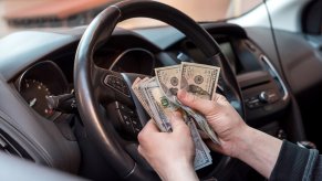 Driver holds a was of cash after buying a new car.