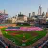 A huge USA national flag unfolded at baseball stadium, the Detroit city skyline visible in the background.