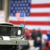 Vintage Jeep truck during a parade, an American flag visible in the background.