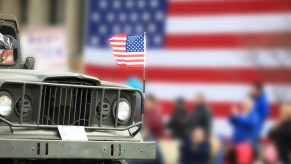 Vintage Jeep truck during a parade, an American flag visible in the background.