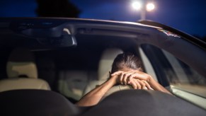 Woman hides behind the steering wheel of her parked car.