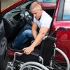 Paralyzed military veteran folding up his wheelchair after getting into a red car.