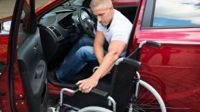 Paralyzed military veteran folding up his wheelchair after getting into a red car.