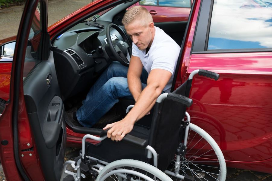 Paralyzed military veteran folding up his wheelchair after getting into a red car.