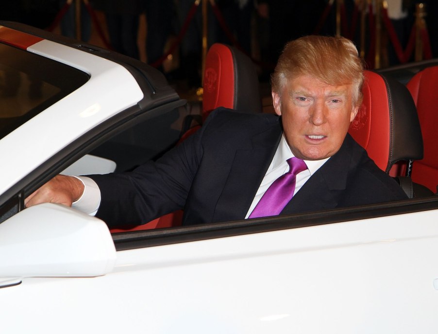 Donald Trump sitting in a white Chevrolet Camaro convertible with a red interior.