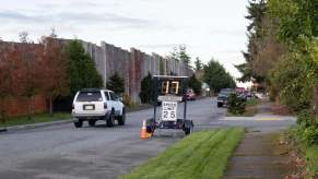 An SUV drives past a speed limit sign with an electronic indicator.