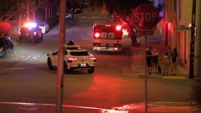 A Waymo self-driving car drives up a road near police and fire vehicles.