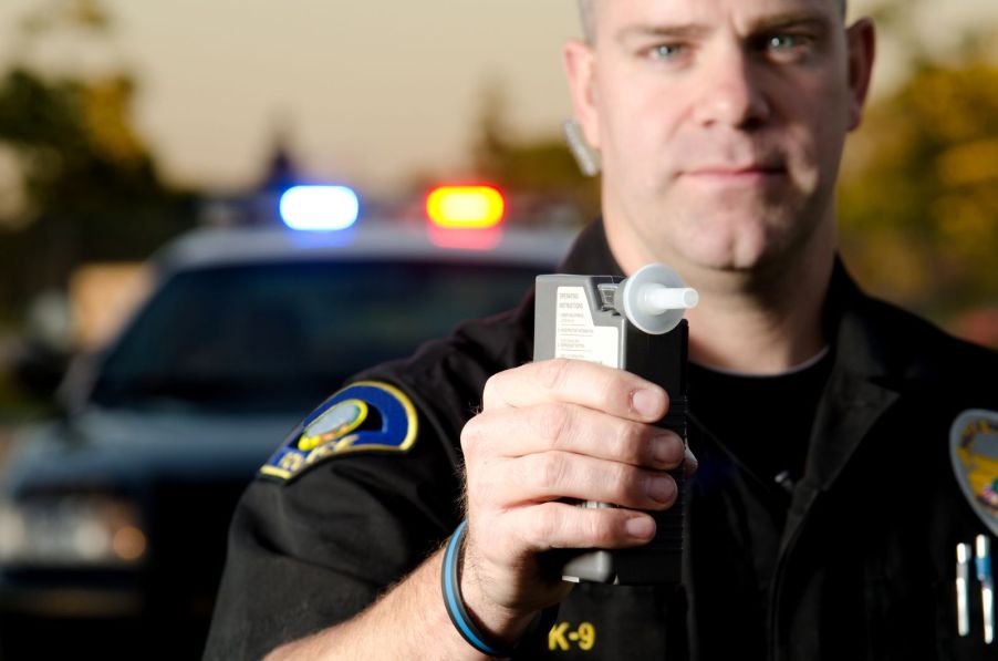 A police officer holding a breathalyzer to a driver to determine if they're driving drunk