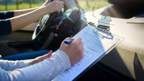 A drivers licensing exam taking place inside a car in close view of the driver and instructor arms