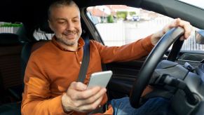 A man holding a phone while driving and smiling at what he sees