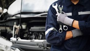 A mechanic standing in front of a car holding wrenches