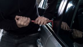 A man attempting to steal a car by using a crow bar against a window to get into the car