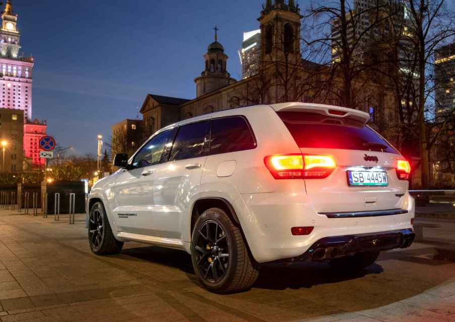 A Jeep Grand Cherokee Trackhawk driving on a public road at night with the taillights illuminated