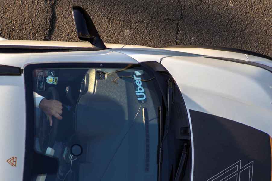 A person driving a car with an "Uber" label in the front window