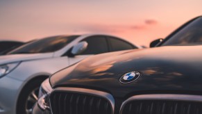 A used BMW parked next to another car at sunset in very close view of the hood